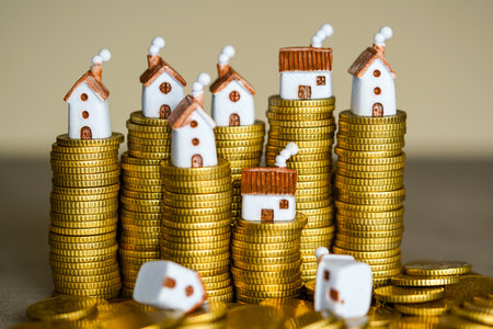 Tiny house models placed on piles of gold coins, symbolizing real estate prices, mortgage loans, housing market trends, savings, and property investmentsの写真素材