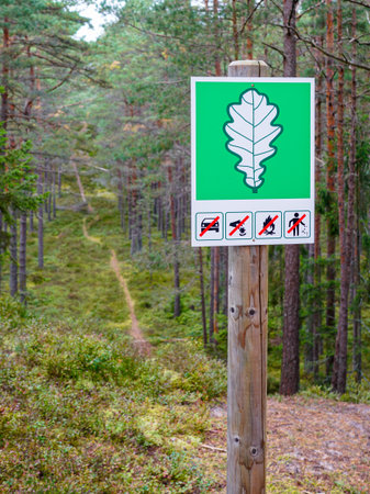 Signpost with oak leaf symbol marks a protected forest area, showing restrictions on driving, fires, littering, and other activities in nature reserveの写真素材