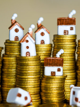 Tiny model houses placed on piles of golden coins, representing property investment, housing finance, mortgage, and real estate wealth buildingの写真素材