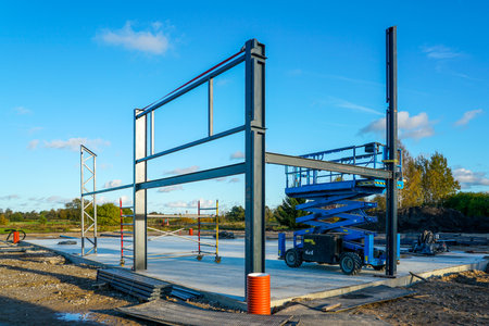 Steel structure under construction with a scissor lift and scaffolding at a building site. Industrial equipment and framework for modern constructionの写真素材