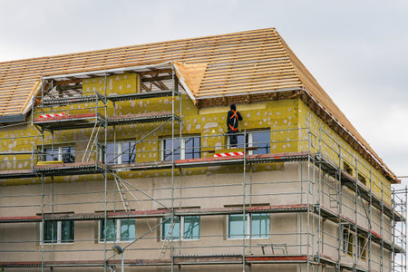 Building under renovation with scaffolding, worker using safety harnesses installing mineral wool facade insulation to improve energy efficiencyの写真素材