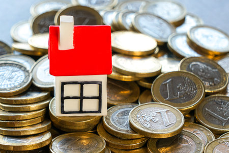 Miniature house with red roof placed on stacks of euro coins. Concept for real estate, mortgage, housing market, savings, investment, and property financeの写真素材