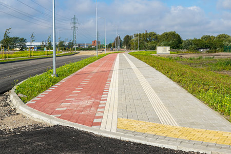Freshly built urban walkway with red and gray paving stones, tactile guidance lines, and modern street lighting in a developing city areaの写真素材