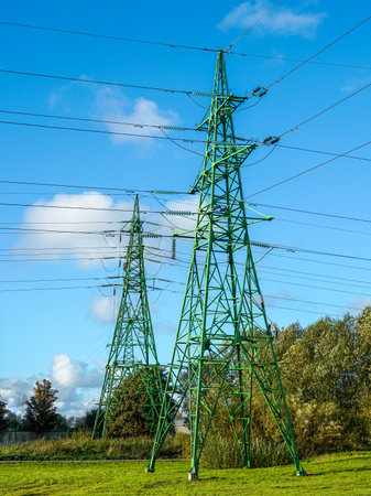 High-voltage green electricity pylons with power lines stretching across a clear blue sky, symbolizing energy, power supply, and infrastructureの写真素材