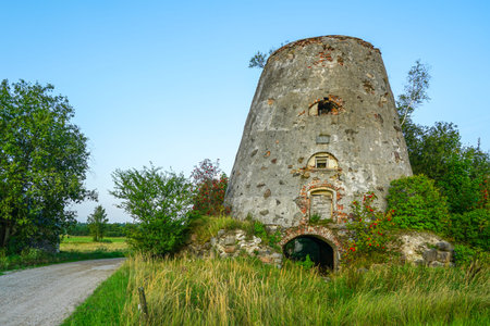 Old stone windmill tower ruin with arched brick doorway, weathered walls, and overgrown greenery...