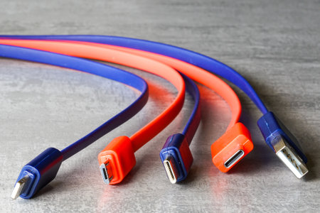 Close-up of red and blue USB, Micro USB, and USB-C charging cables on a gray surface, symbolizing tech, data transfer, and connectivityの写真素材