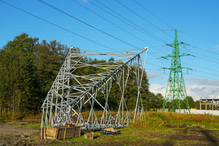 New metal framework of a power transmission tower under construction beside an existing green pylon, symbolizing energy infrastructure and supplyの写真素材