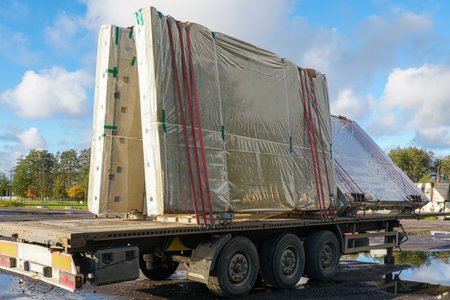Prefabricated concrete wall panels wrapped in protective plastic and tightly strapped on a flatbed truck trailer at a construction logistics siteの写真素材