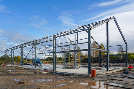 Steel frame of a modern industrial warehouse or factory building under construction, with scaffolding and equipment on siteの写真素材