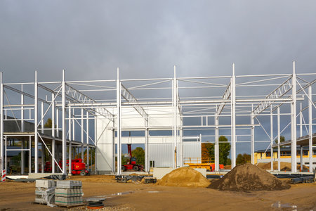 Industrial warehouse construction with white steel frame structure, cranes, and building materials. Modern construction site and development progressの写真素材