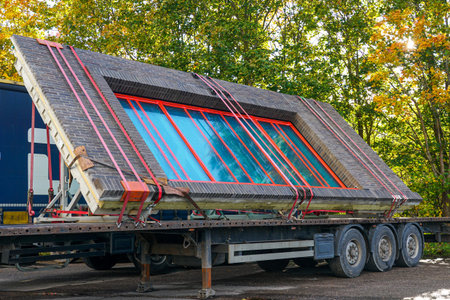 Prefabricated concrete wall with red-framed window loaded on truck trailer, ready for delivery to a modern building construction siteの写真素材