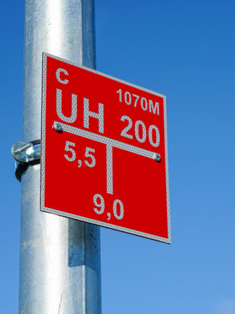Close-up of a red fire hydrant location sign with reflective markings mounted on a metal lighting pole against a clear blue sky for emergency use identificationの写真素材
