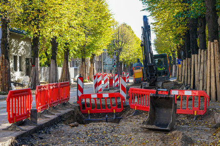 Street reconstruction site with excavator, safety barriers, and protected trees along the sidewalk in an urban area during road maintenance workの写真素材