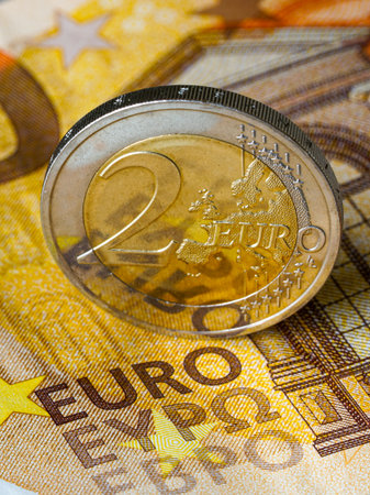 Vertical photo of a two euro coin standing on a fifty euro banknote, representing European currency, finance, economy, savings, and monetary stabilityの写真素材