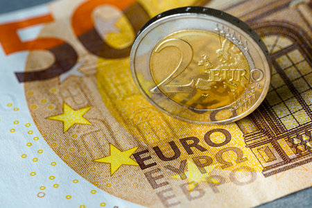 Close-up of a two euro coin standing upright on fifty euro banknote, symbolizing European currency,...