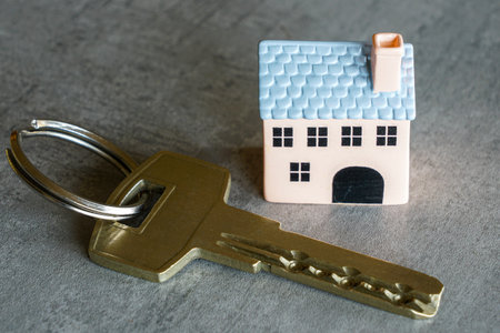 Small house model next to a metal key on a gray surface, symbolizing property ownership, real estate investment, security, and home purchaseの写真素材