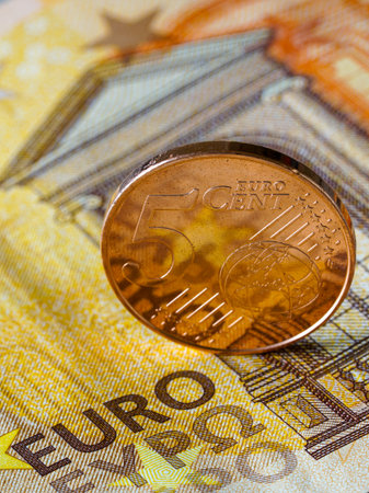 Close-up vertical photo of a five euro cent coin standing on a fifty euro banknote, representing European currency, economy, and financial stabilityの写真素材