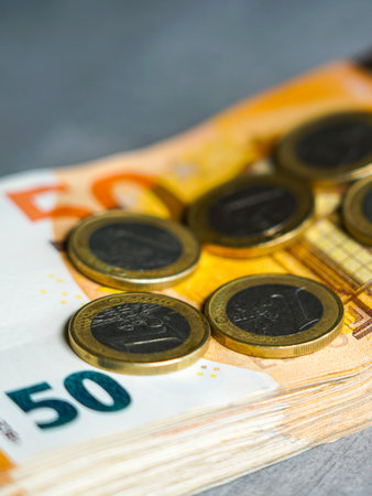 Close-up view of several one euro coins on a stack of fifty euro banknotes, representing finance, savings, investment, and European economic stabilityの写真素材