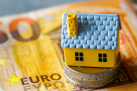 A small yellow house model placed on stacked euro coins and a fifty euro banknote, symbolizing mortgage, home investment, savings, real estate marketの写真素材