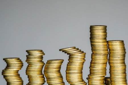 Conceptual image of leaning gold coin stacks representing financial instability, economic imbalance, investment risk and uncertainty in global financeの写真素材