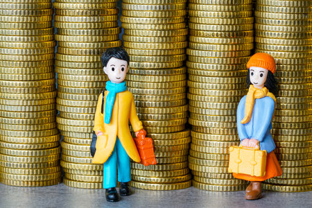 Toy figurines of students with suitcases standing near tall stacks of gold coins, representing rising tuition fees, education expenses, and financial challengesの写真素材