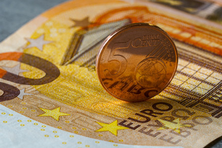Close-up of a five euro cent coin standing upright on a fifty euro banknote, representing European currency, savings, finance, and economic valueの写真素材