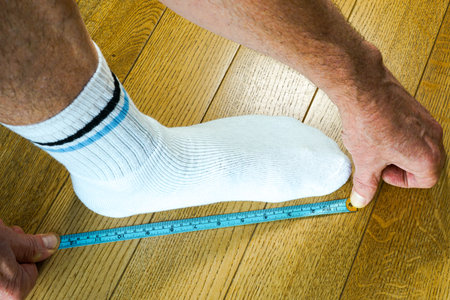 Close-up of a person measuring foot length in socks using a ruler marked in centimeters and inches on a wooden floor to determine shoe size accuratelyの写真素材