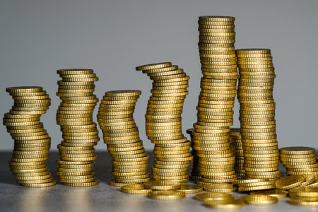 Conceptual image of leaning stacks of gold coins representing financial instability, economic imbalance, market volatility, and uncertain investment conditionsの写真素材