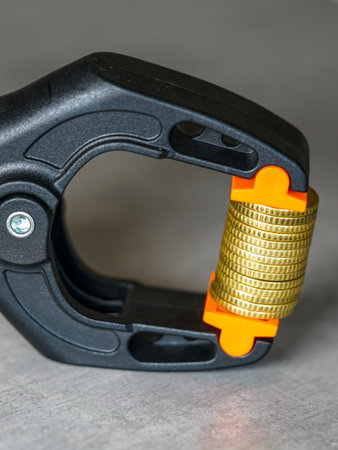 Close-up of gold coins tightly clamped in a black and orange tool, representing money pressure, financial stress, inflation, and economic crisis conceptの写真素材