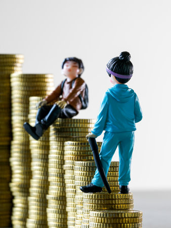 Two miniature figures stand on uneven stacks of golden coins, symbolizing financial inequality, economic gap, the concept of success and opportunityの写真素材
