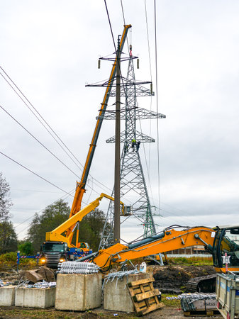 Workers and cranes install high-voltage transmission tower at construction site, showing teamwork, engineering precision, modern energy infrastructureの写真素材