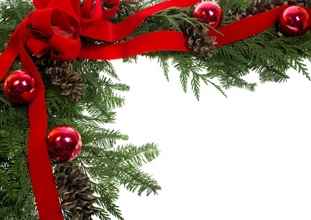 A decorative border of pine boughs ornaments cones ribbon and bow isolated on whiteの写真素材
