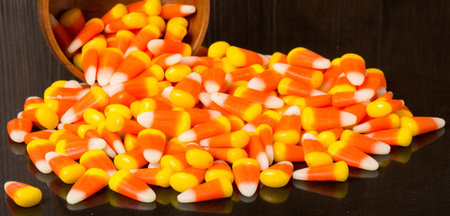 Candy corn spilling from wooden bowl onto black table