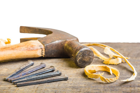 A hammer and nails on a wood board with sawdust shavings
