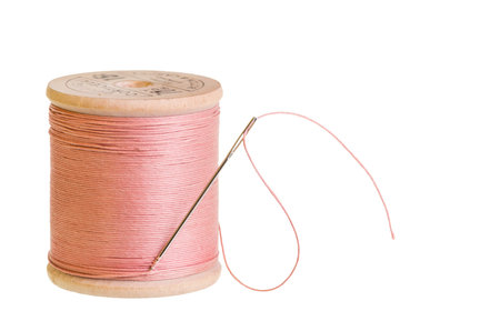 A spool of pink sewing thread with a needle on white