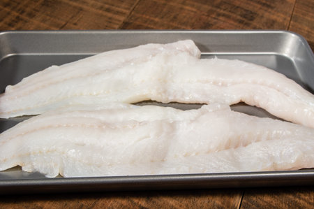 Two fillets of fresh cod fish on a baking pan