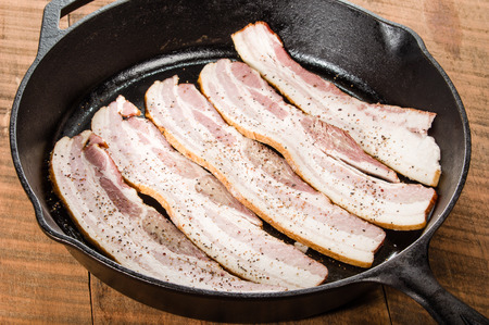 Cast iron skillet with strips of raw bacon ready to fryの写真素材