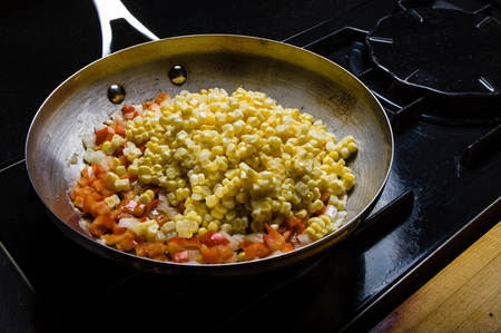 Sweet corn red peppers and onions in fry pan on the stoveの写真素材
