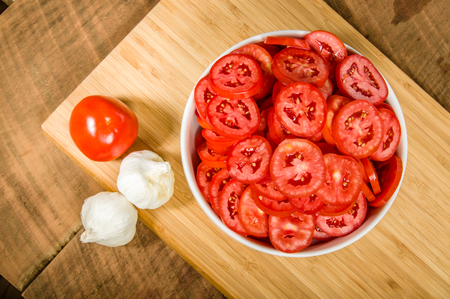 Garlic cloves and bowl of red sliced tomatoesの写真素材