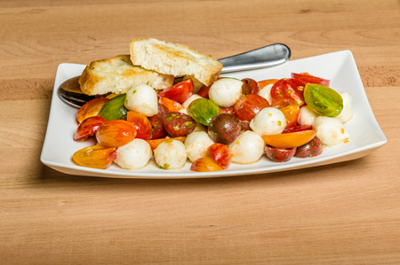 Fresh heirloom tomatoes with cheese served with bread on plateの写真素材
