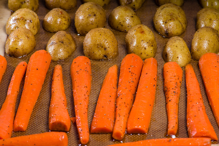 Potatoes and carrots on a baking sheet ready for the ovenの写真素材