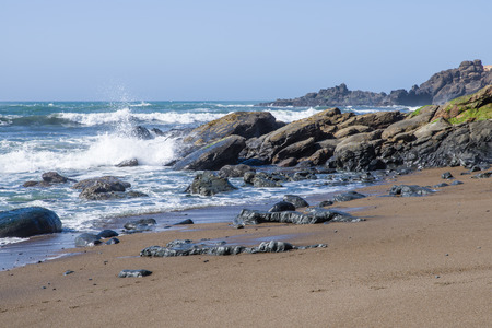Surf and waves on a rocky coast with grey overcast skiesの写真素材