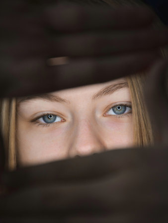 Young woman looking through the blinds at the camera. Focus on the eyes.の写真素材