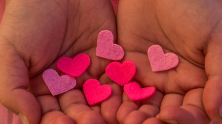 Children's hands holding the heart on a pink background. Concept of love, care, faith, hope, purityの写真素材