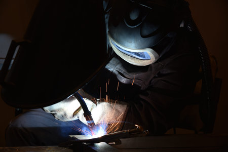 worker with protective mask welding metal and sparks. The welder is welding metal.