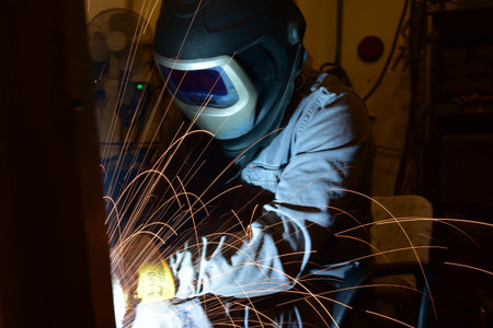 worker with protective mask welding metal and sparks. The welder is welding metal.