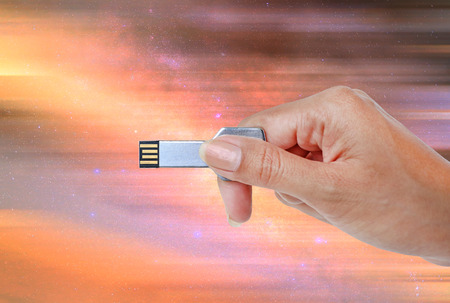 Hand holding USB data storage against bright light and circuit background.の写真素材