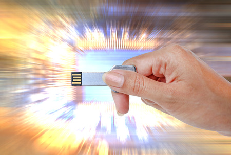 Hand holding USB data storage against bright light and circuit background.の写真素材