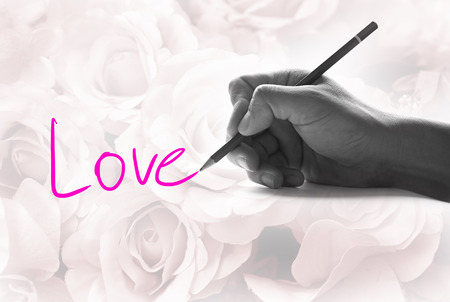 Hand holding a pencil on a vintage rose background, writing for word " Love "の写真素材