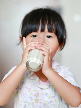 Little girl in pajamas drinking milk from glass indoor at the morning.の写真素材